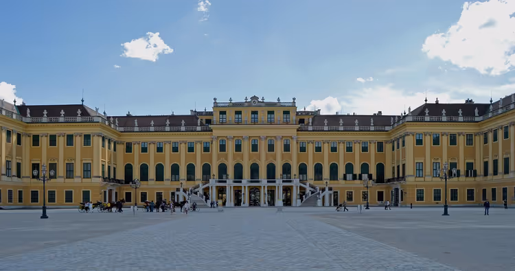 Gelbe Barockfassade von Schloss Schönbrunn in Wien mit weitem gepflastertem Hof unter blauem Himmel