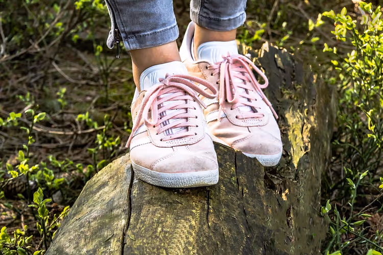 Bein i jeans og rosa joggesko på en trestubbe