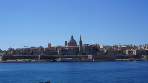 Skyline von Valletta über tiefblauem Wasser mit großer Kirchenkuppel und schlanker Turmspitze über Festungsmauern aus Kalkstein