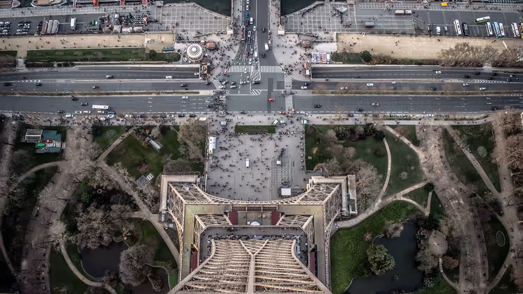 Blick senkrecht vom Eiffelturm in Paris hinab auf seinen Eisensockel, Menschenmengen auf dem Platz, Gärten und Straßen