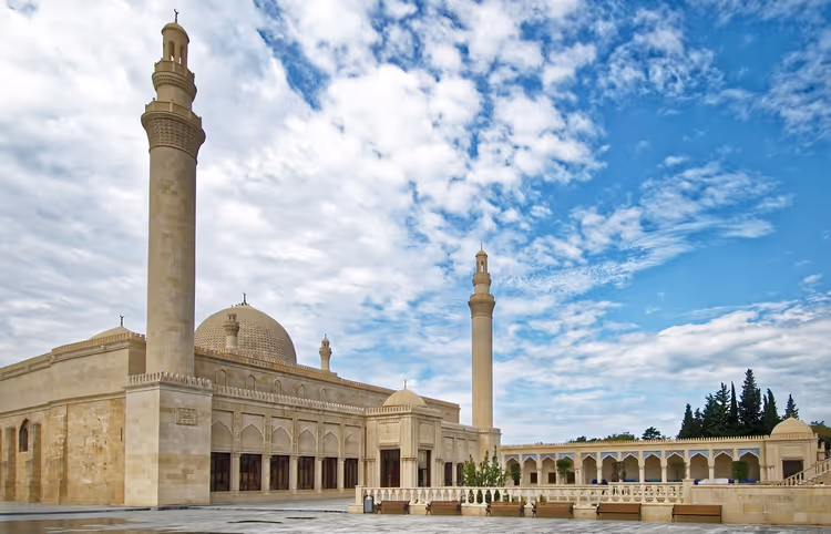 Meczet z piaskowca z dwoma wysokimi minaretami, żebrowaną kopułą i dziedzińcem z arkadami pod pochmurnym niebem w Azerbejdżanie