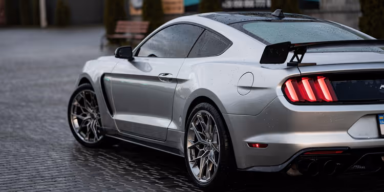 Zilveren Ford Mustang sportwagen op natte kasseien