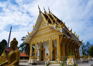 Weiß-goldener buddhistischer Tempel mit gestuftem, verziertem Dach und goldener Buddha-Statue im Vordergrund auf Koh Samui