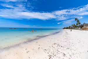 Breiter weißer Sandstrand auf Sansibar mit flachem türkisfarbenem Wasser, Badenden, Holzbooten und Palmen