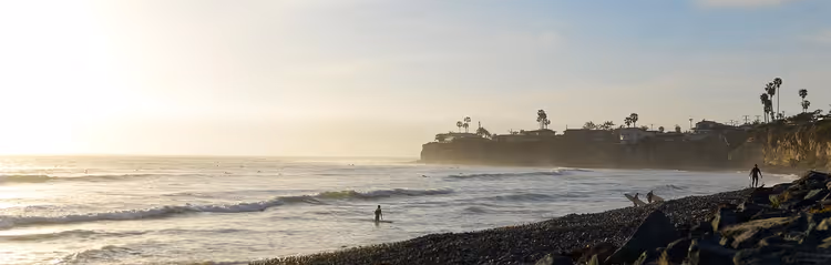 Surfer med brett i solnedgang på kysten av California