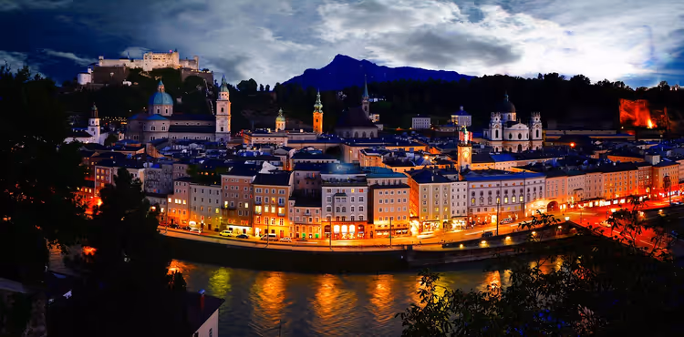 Nattpanorama av Salzburg med elv og festning