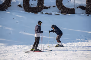 Zwei Skifahrer mit Helmen und Stöcken auf einer präparierten, sonnigen Piste in einem Skigebiet in Andorra