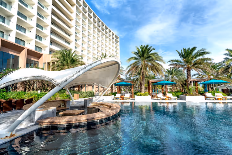 Resortzwembad met cabana's, ligbedden en palmbomen naast het hotel