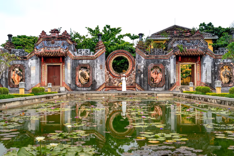 Reich verziertes Tempeltor mit rundem Mondtor und Reliefs in Vietnam, gespiegelt in einem Seerosenteich