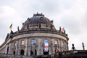 Bode-Museum mit Kuppel auf der Berliner Museumsinsel unter bedecktem Himmel, Banner zwischen den Säulen und Fahnen auf dem Dach