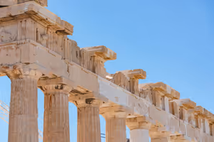 Verwitterte dorische Marmorsäulen und Gebälk des Parthenon vor klarem blauem Himmel in Athen