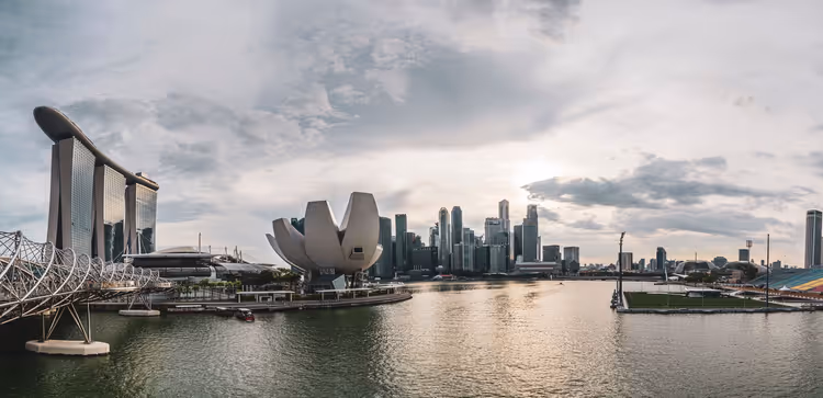 Marina Bay in Singapur unter bewölktem Himmel, mit Marina Bay Sands, dem lotusförmigen Museum und den Hochhäusern der Innenstadt