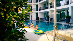 Familie mit kleinem Kind am Rand eines Pools im Hotelinnenhof, umgeben von weißen Gebäuden mit Balkonen