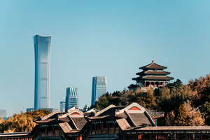 Traditioneller chinesischer Pavillon und Ziegeldächer zwischen Herbstbäumen, dahinter moderne Wolkenkratzer in Peking