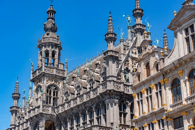 Reich verzierte neugotische Fassade mit Türmchen und vergoldeten Statuen an der Grand-Place in Brüssel unter klarem blauem Himmel