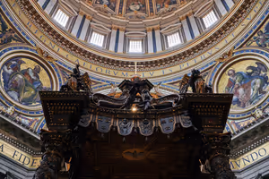Sommità del baldacchino in bronzo sotto la cupola della Basilica di San Pietro a Roma, con mosaici e un'iscrizione latina dorata