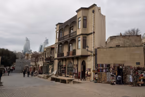 Altes Steinhaus mit Holzbalkonen und Souvenirständen in der Altstadt von Baku, dahinter ragen die Flame Towers auf