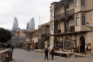 Kopfsteinpflastergasse mit Souvenir- und Teppichläden in der Altstadt von Baku, dahinter ragen die Flame Towers auf