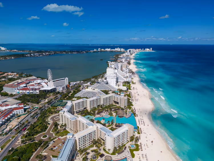 Luftaufnahme der Hotelzone von Cancún mit Resortpools zwischen weißem Sandstrand, türkisfarbenem Meer und einer Lagune