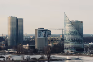Moderne Glastürme und ein Baukran am Flussufer in Riga, Eis auf dem Wasser im weichen Abendlicht