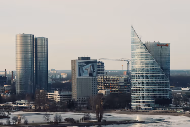 Moderne Glastürme und ein Baukran am Flussufer in Riga, Eis auf dem Wasser im weichen Abendlicht