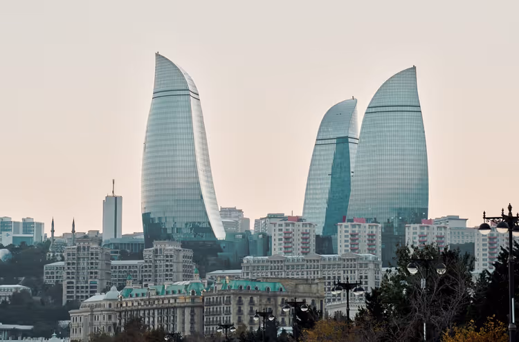 Drei geschwungene gläserne Flame Towers über Wohnblöcken und Gebäuden mit grünen Dächern in Baku unter blassem Himmel
