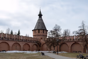 Rote Backsteinmauer des Kremls und ein Rundturm mit hölzernem Zeltdach in Tula, Schneereste unter grauem Himmel