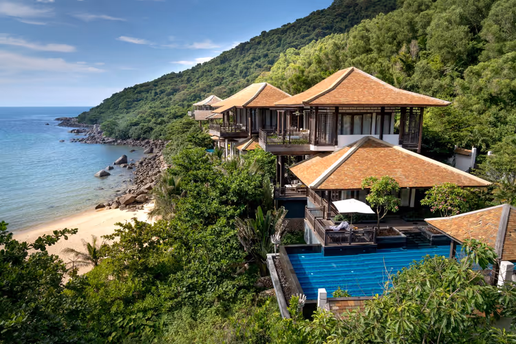 Villen am Hang mit Terrakottadächern und einem blauen Pool über einer kleinen Sandbucht und dschungelbewachsenen Hängen