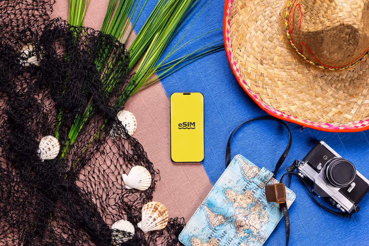 Smartphone mit eSIM und Reiseutensilien auf blauem Hintergrund