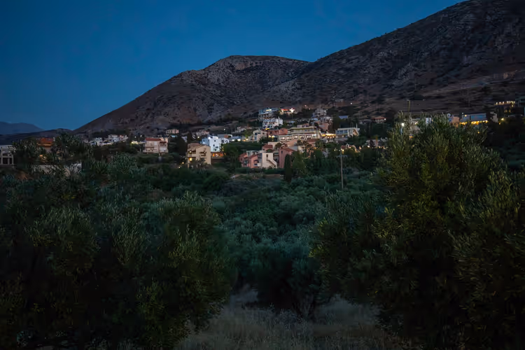 Blick auf das Dorf Hersonissos in der Abenddämmerung zwischen Olivenhainen und Hügeln