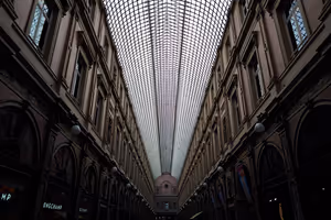 Välvt glastak i en täckt shoppinggalleria i Bryssel, sett underifrån mellan rader av dunkla fasader