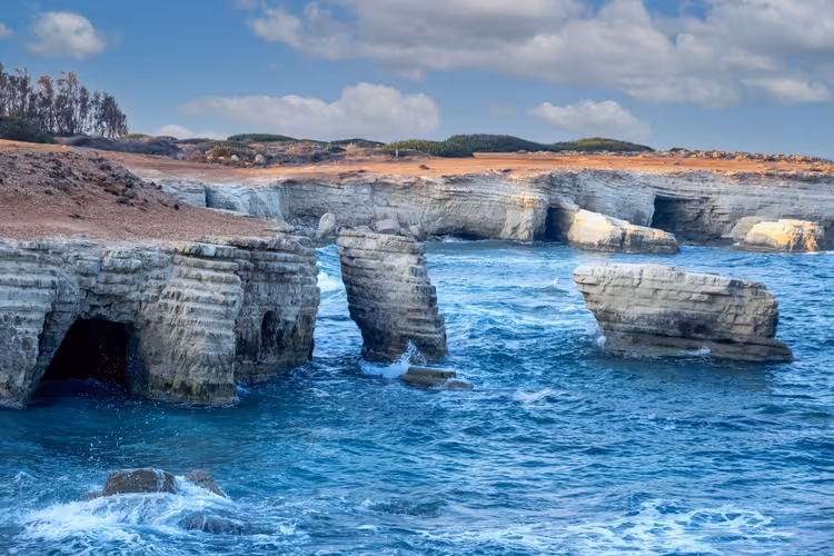 Geschichtete Kalkstein-Meereshöhlen und ein Felsbogen, umspült von blauen Wellen, an der Küste bei Paphos auf Zypern