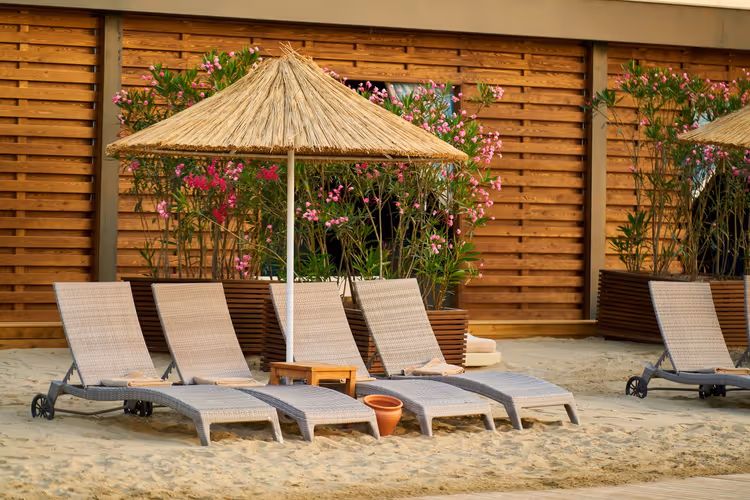 Ligstoelen en een rieten parasol op het zand bij het hotel