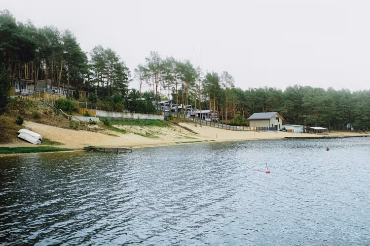 Lago, margem arenosa e cabanas na floresta