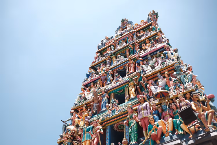 Gestufter Gopuram-Turm des Sri Mariamman Temple in Singapur, bedeckt mit bemalten Statuen hinduistischer Gottheiten, vor blassem Himmel