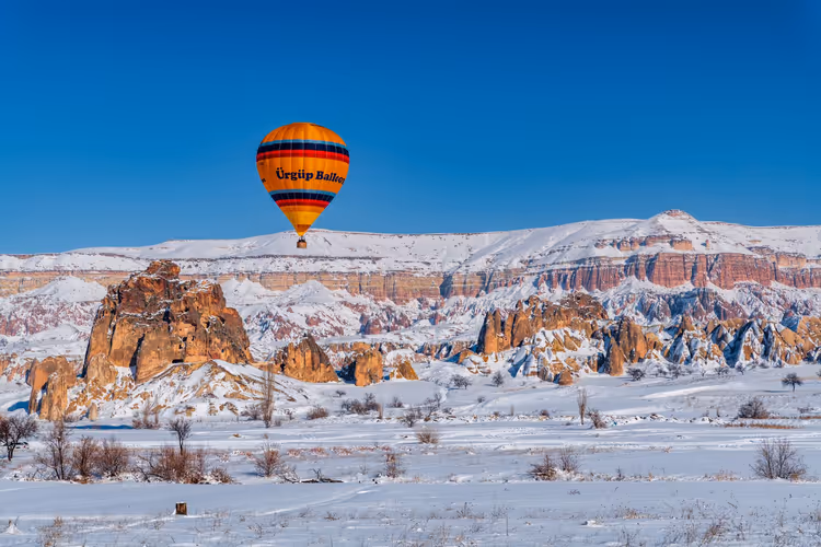 Hot air balloon over snowy Cappadocia rock formations
