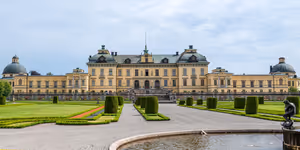 Gelbes Barockschloss mit überkuppelten Seitenpavillons hinter einem formalen Garten mit geschnittenen Hecken und Brunnen bei Stockholm