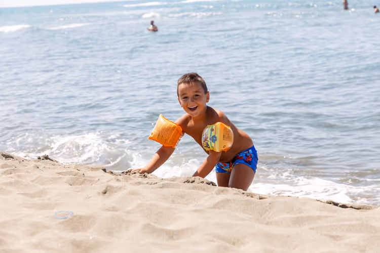 Lachend kind met zwembandjes op een zandstrand