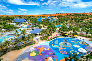 Luftaufnahme eines großen Wasserparks mit buntem Wasserspielplatz, Rutschen, Pavillons mit blauen Dächern und Palmen