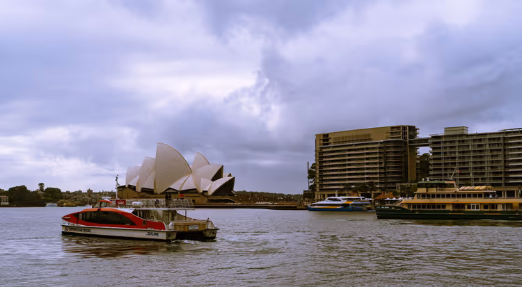 Fähren im Hafen von Sydney vor den Segeln des Opernhauses unter schweren grauen Wolken