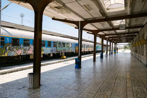 Leerer Bahnsteig mit gefliestem Boden und eisernem Vordach neben einem mit Graffiti bedeckten Personenzug