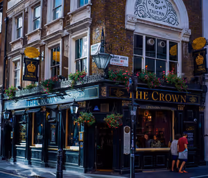 Façade noire et dorée du pub The Crown à un angle de rue à Londres, avec des paniers de fleurs suspendus et des étages en brique