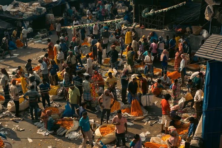 Belebter Straßenblumenmarkt in Indien von oben, mit Händlern und Bergen orangefarbener Tagetes-Girlanden