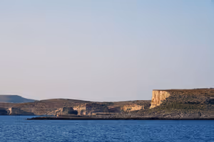 Niedrige Kalksteinklippen und ein karges Felsufer im warmen Abendlicht über dem tiefblauen Meer auf Malta