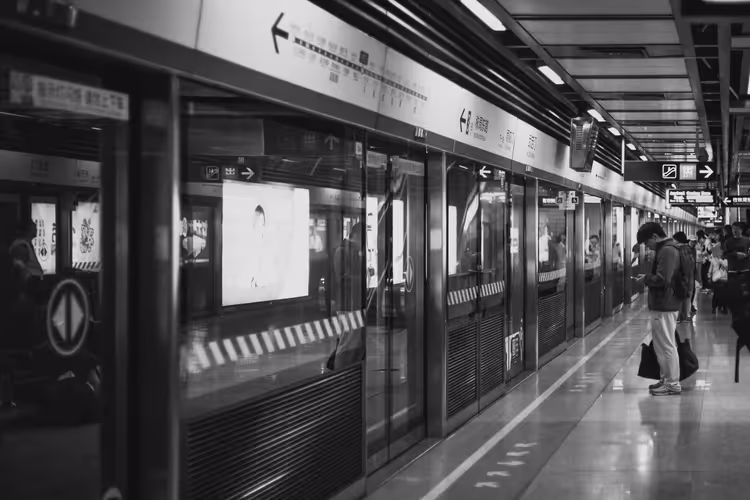 Schwarz-weiß gestalteter U-Bahnsteig in China mit gläsernen Bahnsteigtüren und einem Fahrgast, der aufs Handy schaut