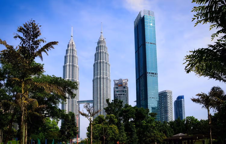 KLCC Parkı'nın ağaçları üzerinde Petronas Kuleleri ve gökdelenler
