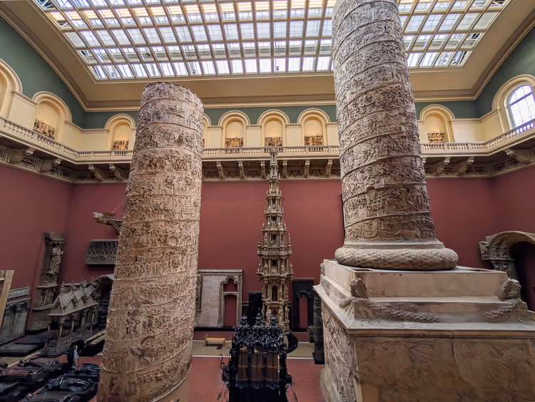 Zwei hoch aufragende Gipsabgüsse einer römischen Reliefsäule in einem Museumssaal mit roten Wänden und Glasdach