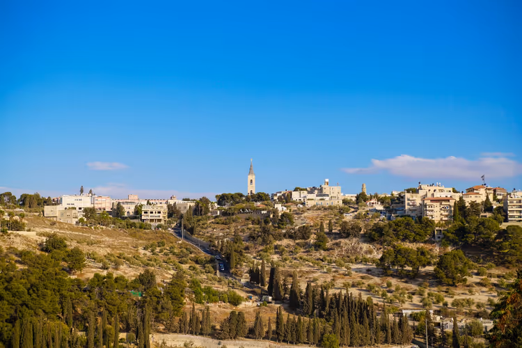 Stadt am Hang in Israel mit schlankem Kirchturm, hellen Steinhäusern und Zypressen unter klarem blauem Himmel