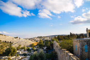 Alte steinerne Stadtmauer und ein Minarett über Friedhöfen am Hang und Zypressen in Jerusalem