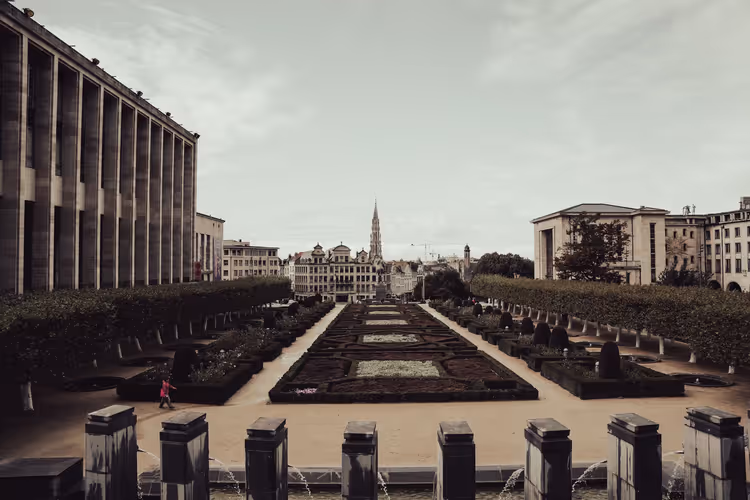 Formaler Garten am Mont des Arts in Brüssel mit gestutzten Hecken, Brunnen und der Rathausspitze unter bedecktem Himmel